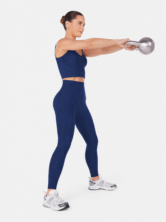 Easelyn Built-In Resistance Band Leggings in Navy, full-body side view swinging a kettlebell, print side with tonal band lines