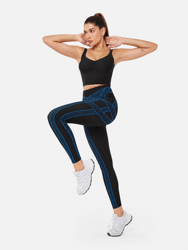 Easelyn Built-In Resistance Band Leggings in Black/Power Blue, full-body front view with one knee raised, showing the power blue band lines