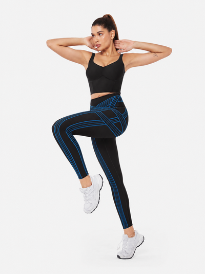Easelyn Built-In Resistance Band Leggings in Black/Power Blue, full-body front view with one knee raised, showing the power blue band lines