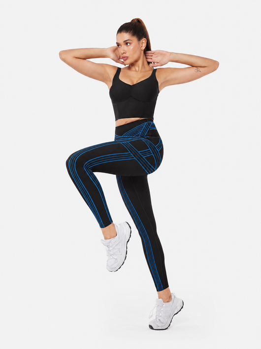 Easelyn Built-In Resistance Band Leggings in Black/Power Blue, full-body front view with one knee raised, showing the power blue band lines