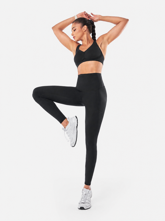 Easelyn Built-In Resistance Band Leggings in Black, full-body view balancing on one leg with arms overhead, solid reverse side