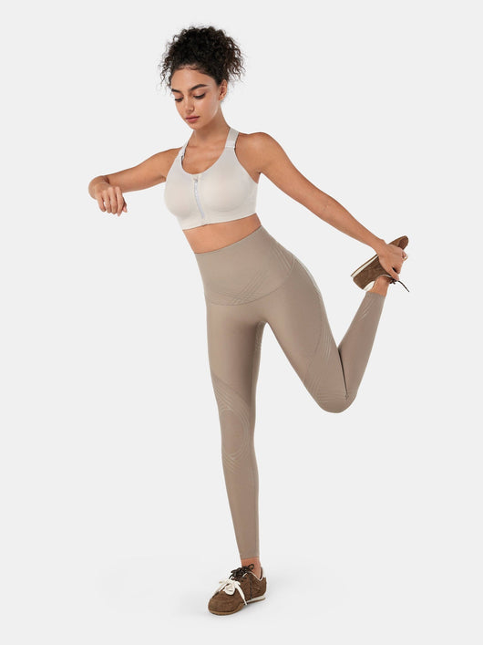 Easelyn Postpartum Recovery Compression Leggings in Tan, full-body standing quad stretch showing the high compression waistband