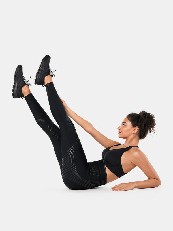 Easelyn Postpartum Recovery Compression Leggings in Black, floor core exercise with both legs raised, showing the compression lines along the back of the legs