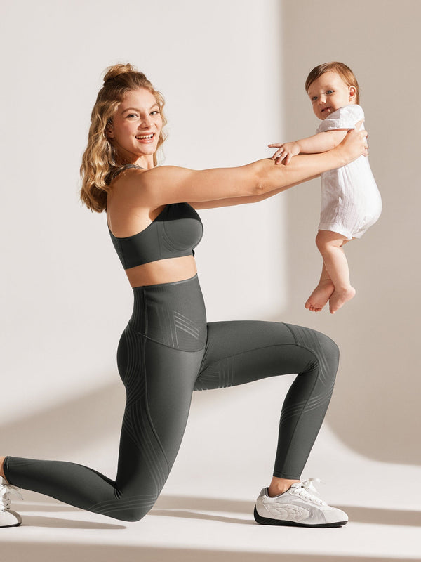 Easelyn Postpartum Recovery Compression Leggings in Dark Gray, kneeling lunge while lifting a baby, showing the contoured compression lines