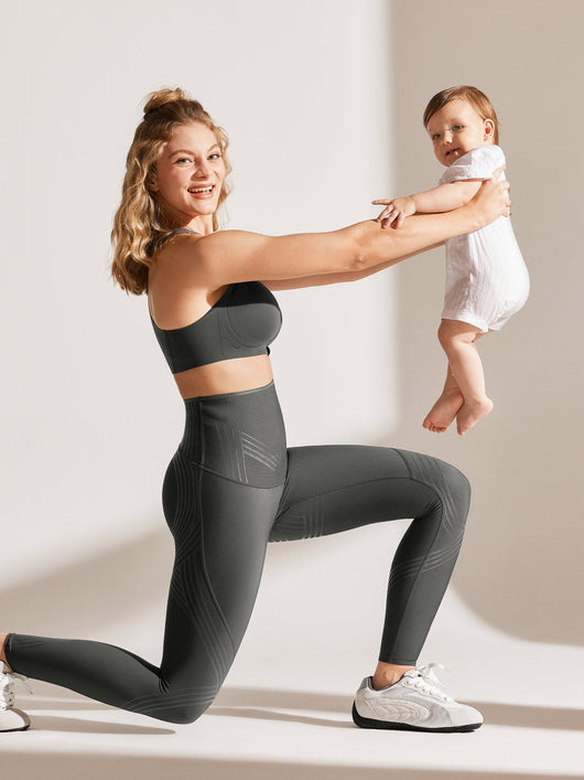 Easelyn Postpartum Recovery Compression Leggings in Dark Gray, kneeling lunge while lifting a baby, showing the contoured compression lines