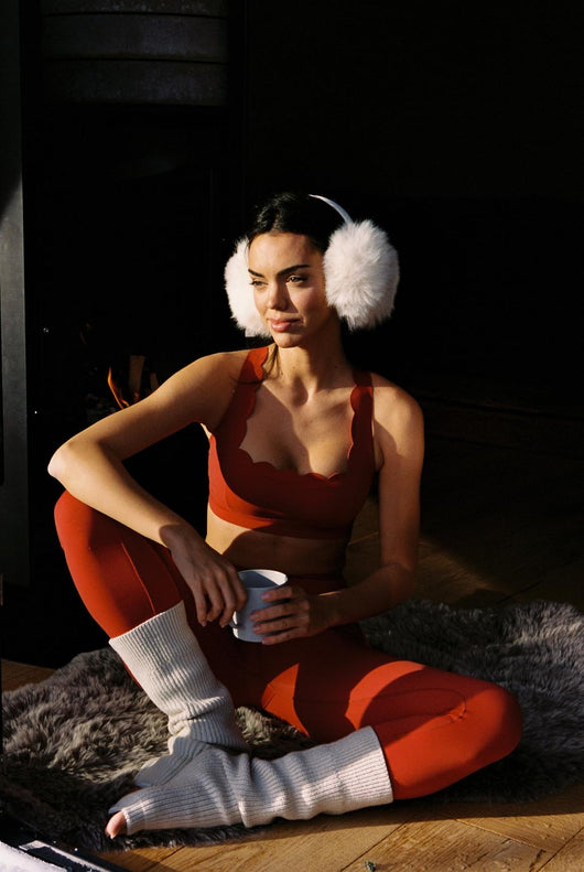 Easelyn Classic Cross-Back Sports Bra in Fire Cracker, seated by the fireplace holding a mug