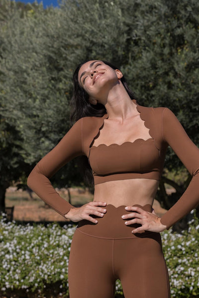 Easelyn Scallop-Edge Long-Sleeve Workout Crop Top in Roasted Cocoa, Mini length, hands on hips in a sunny olive garden