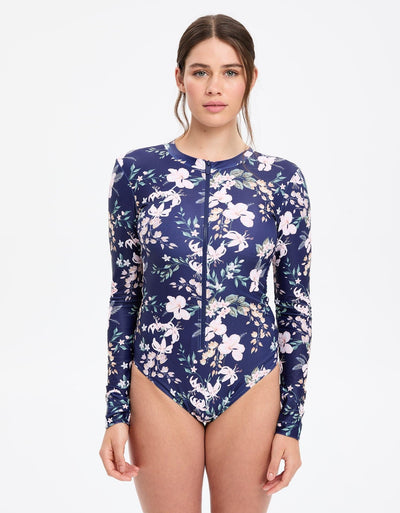 Easelyn UPF 50+ Long-Sleeve One-Piece Swimsuit in Tropical Navy Floral, front view on model showing the front zipper and scoop high neckline